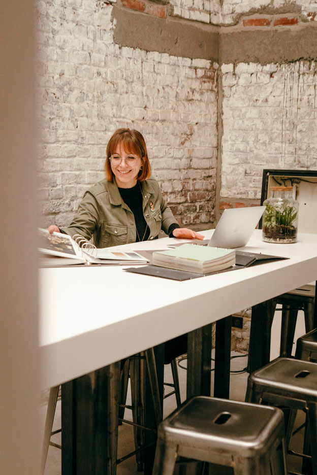 Architecte d'intérieur Amandine, fondatrice de Madame Dek, examinant des plans de design dans un espace de travail chaleureux, illustrant son approche personnalisée de l’aménagement intérieur